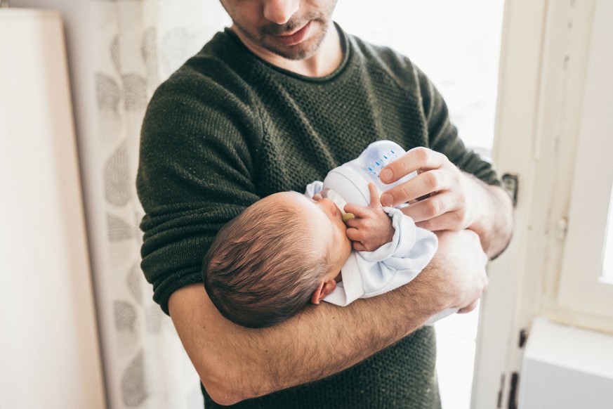 Unrecognizable man feeding newborn baby boy with milk in baby bottle, close up