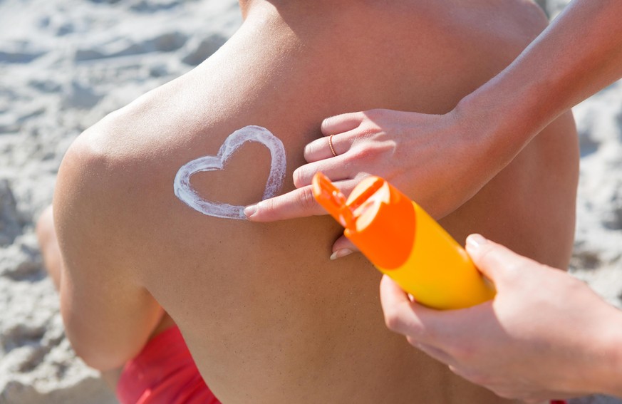 High angle view of woman making heart shape with sunscream on man back at beach during sunny day || Modellfreigabe vorhanden