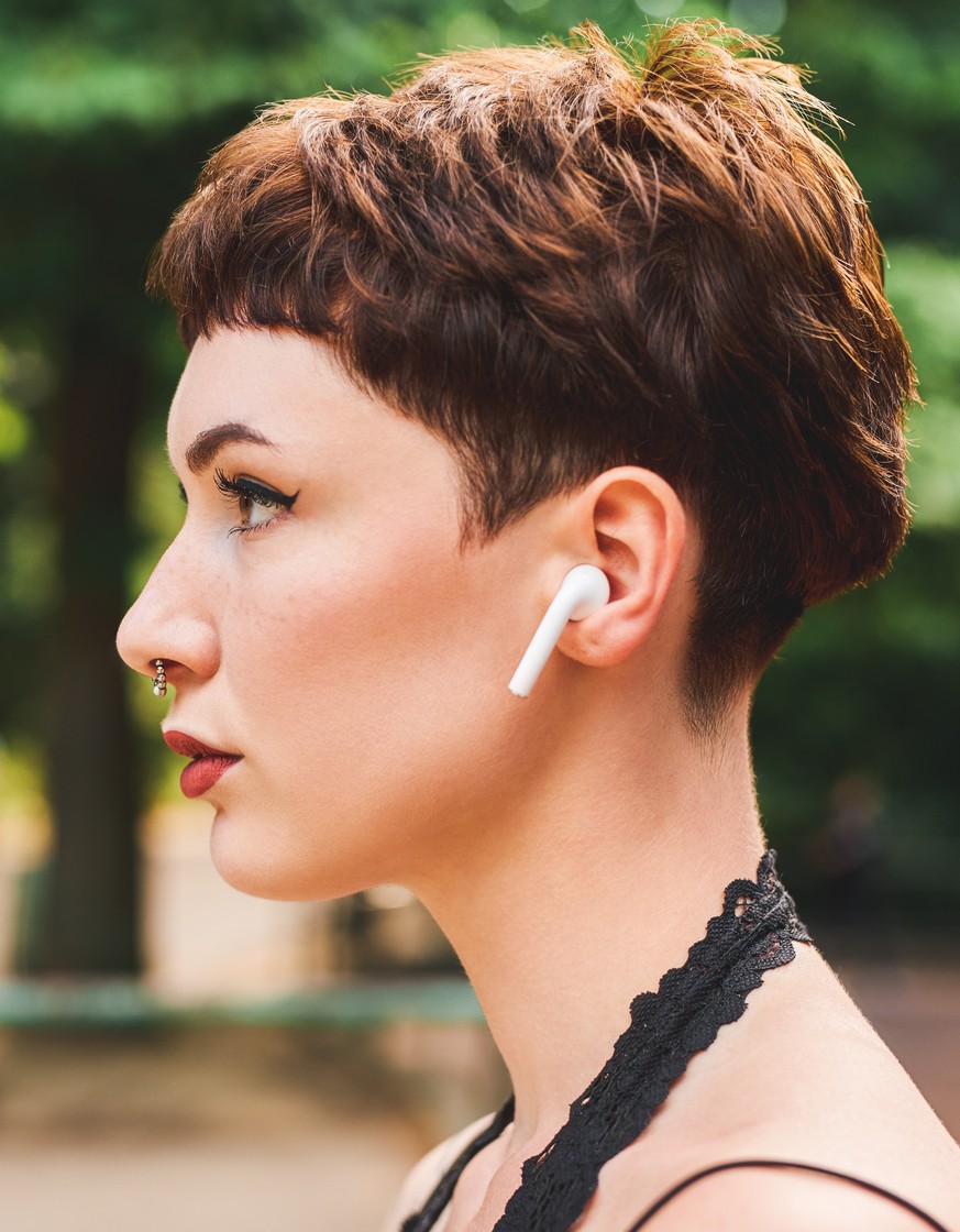 Cropped shot of an attractive young woman listening to music on her airpods while standing in a park during the day