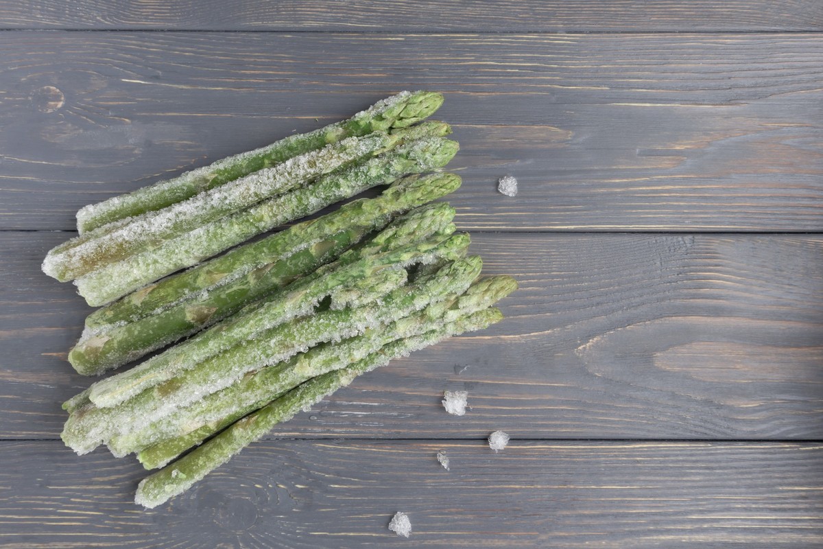 Frozen asparagus on a wooden surface with space for text. Article.