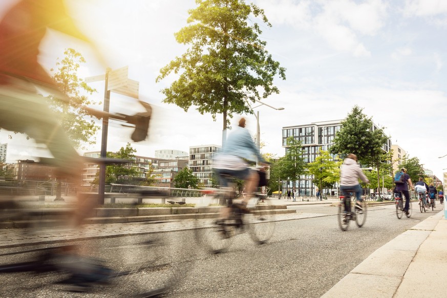 Motion blurred cyclists riding inside a city on a sunny day.