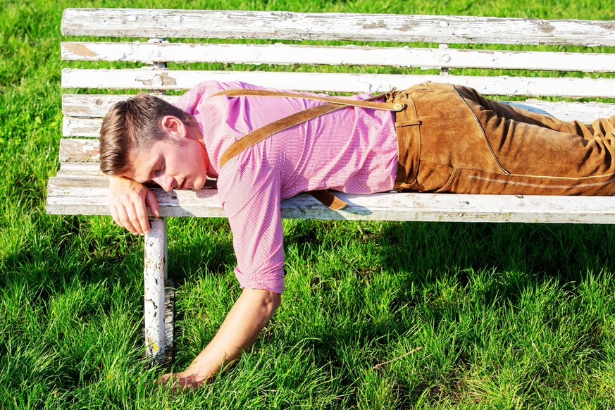 handsome blond bavarian man sleeping outdoors on a bench