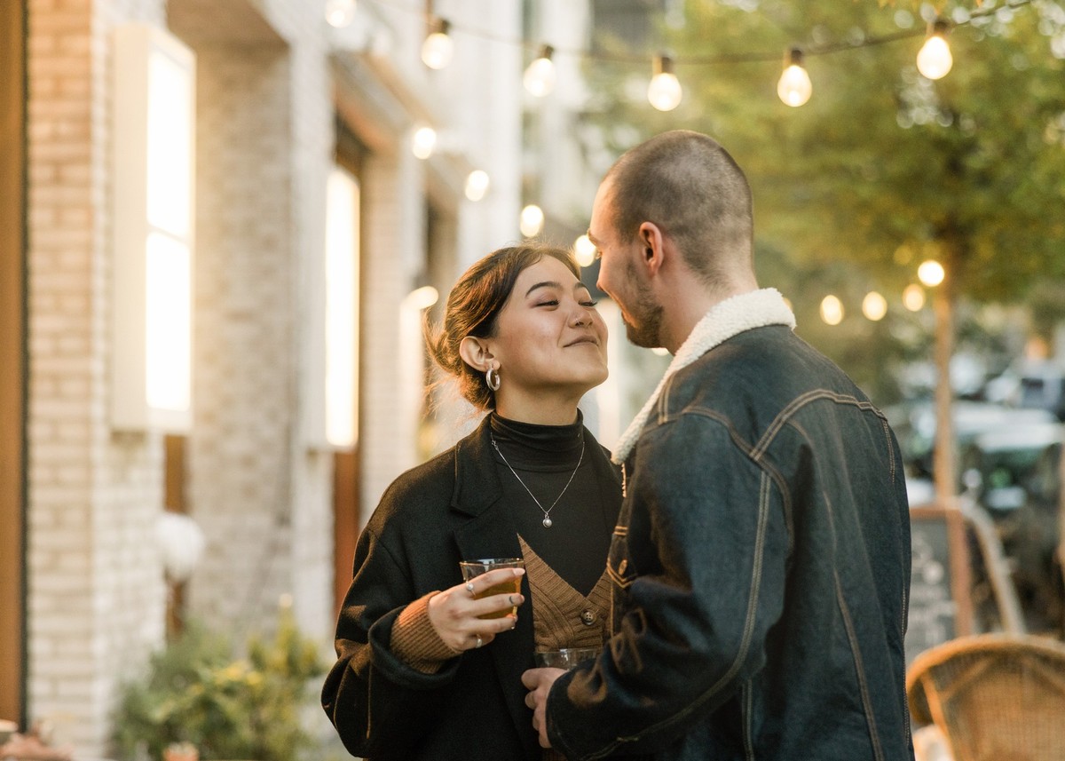 Couple in love about to kiss outside a coffee shop in the city. Young man and woman holding a tea about to kiss outdoors in a winter evening.