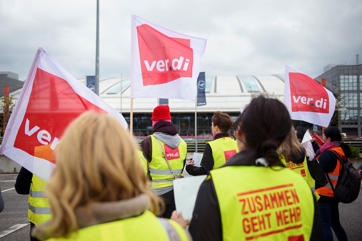 24.04.2023, Hamburg: Mitarbeiter und Mitarbeiterinnen der Aviation Handling Services GmbH (AHS) stehen mit Fahnen und Warnwesten während einer Kundgebung im Rahmen eines Warnstreiks auf einem Parkplat ...