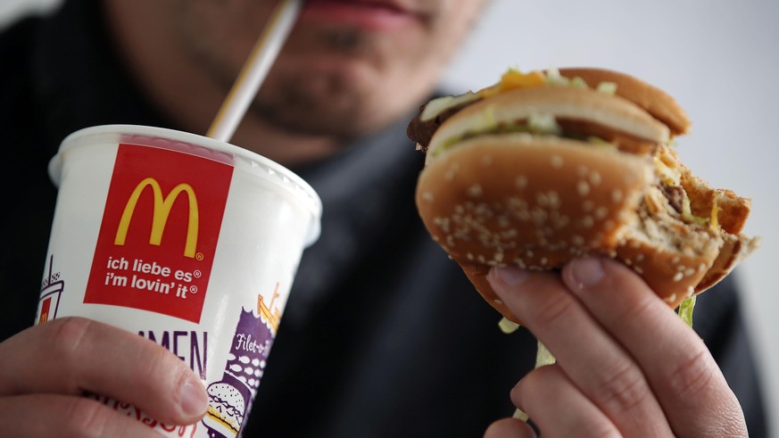 A man drinks a coke and eats a Big Mac burger at a branch of fast food franchise McDonalds in Cologne, Germany, 25 May 2015. Photo: Oliver Berg/dpa