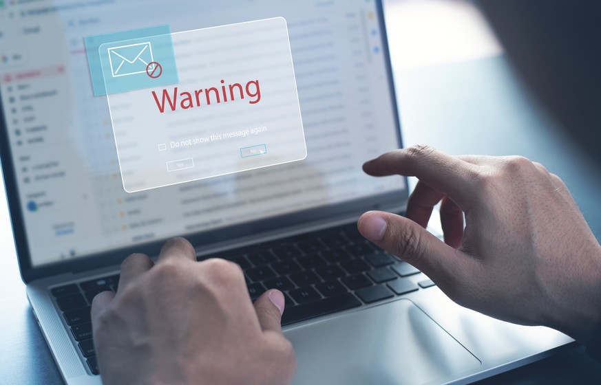 Blocking spam e-mail, warning pop-up for phishing mail, network security concept. Business man working on laptop computer at home with warning window on screen