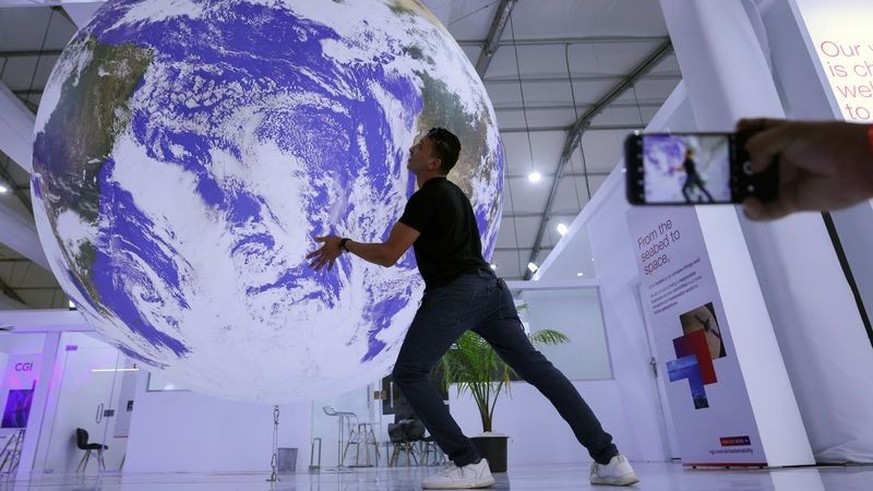 An attendee poses for a picture near a model earth during the COP27 climate summit in Sharm el-Sheikh, Egypt November 19, 2022. REUTERS/Mohamed Abd El Ghany