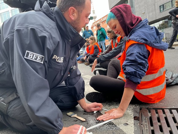 Es dauerte eine Weile, bis die Polizei die festgeklebten Hände der Aktivist:innen von der Straße lösen konnte.