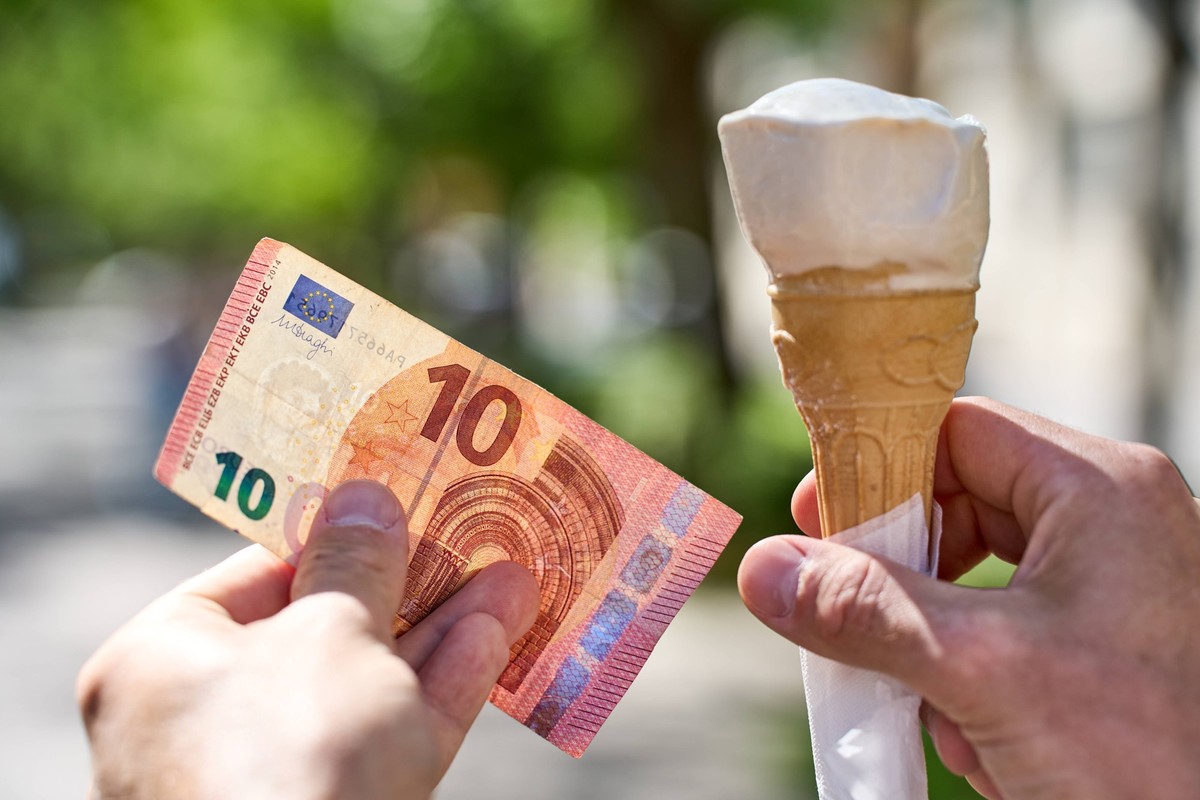 Ancona, Italy - May 10, 2024: Hand holding an ice cream in a waffle next to a 10 euro banknote. Symbolic image cost and increase for the price of a scoop of ice cream *** Hand hält ein Eis in einer Wa ...
