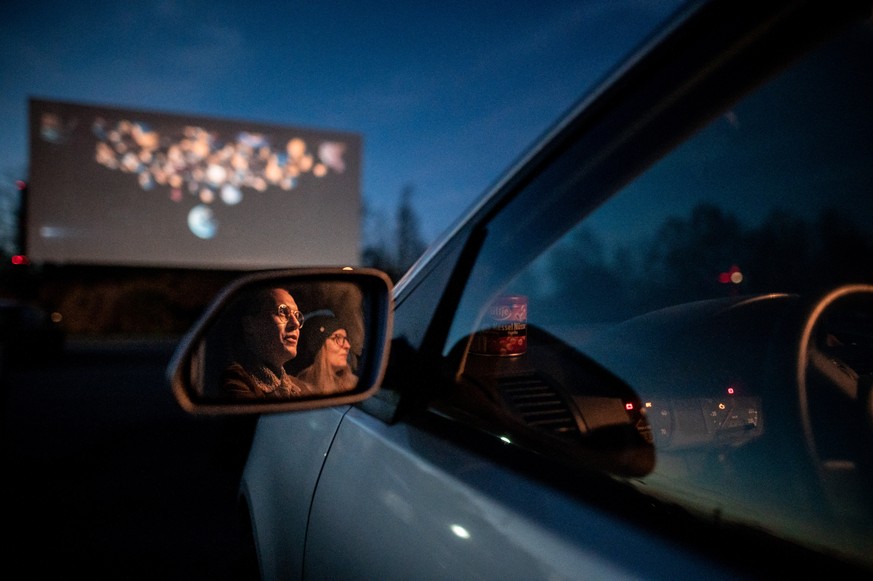 24.03.2020, Nordrhein-Westfalen, Essen: Zwei Besucher des Autokino sitzen im Auto und gucken auf die Leinwand. Das Kino hat auch w