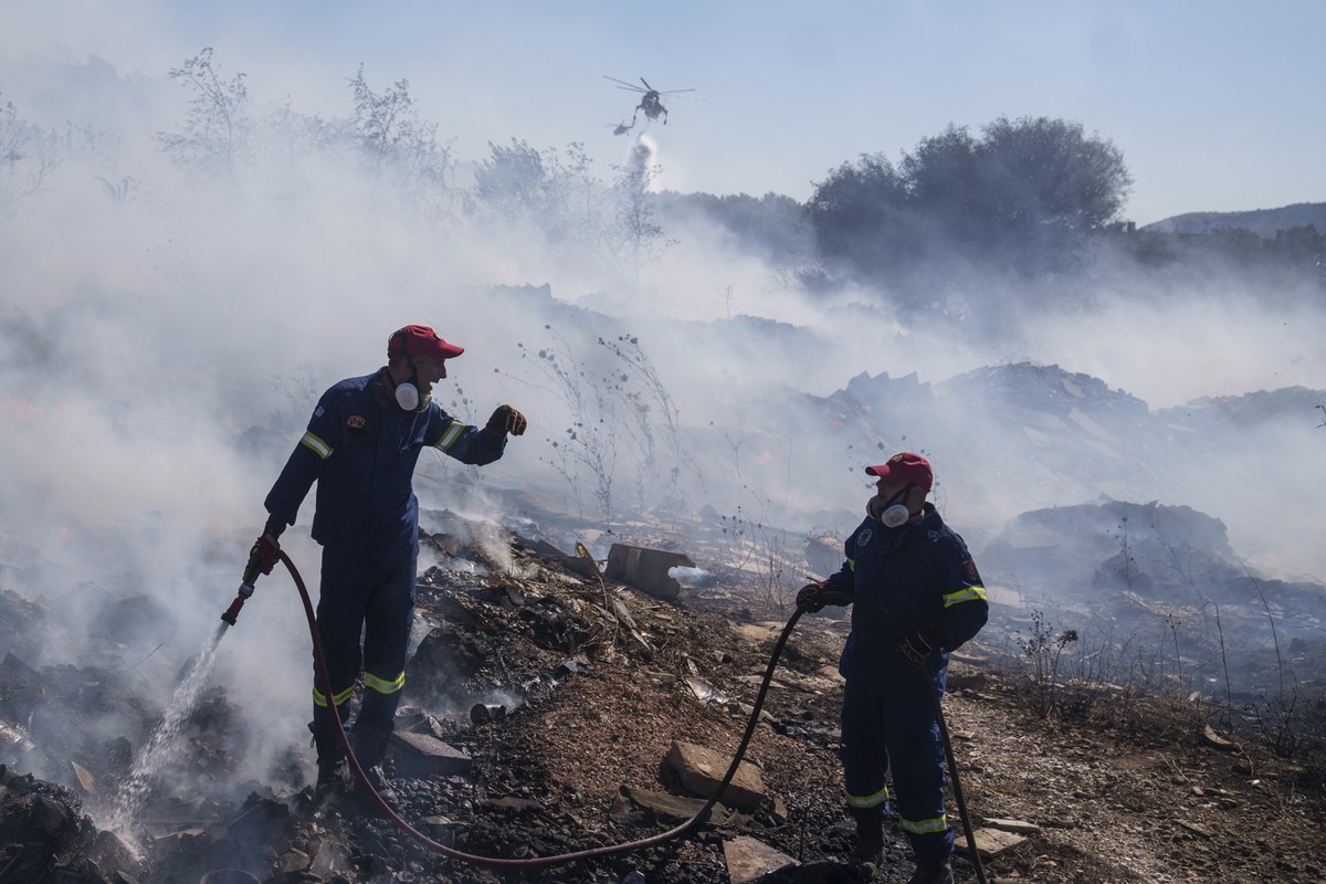 20.06.2024, Griechenland, koropi: Feuerwehrleute versuchen, ein Feuer zu löschen, während ein Löschhubschrauber Wasser im Vorort Koropi im Osten von Athen abwirft. Foto: Petros Giannakouris/AP/dpa/dpa ...