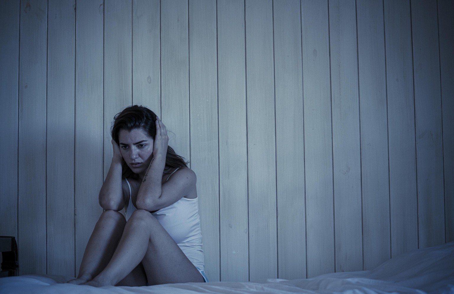Sad young woman sitting on bed || Modellfreigabe vorhanden