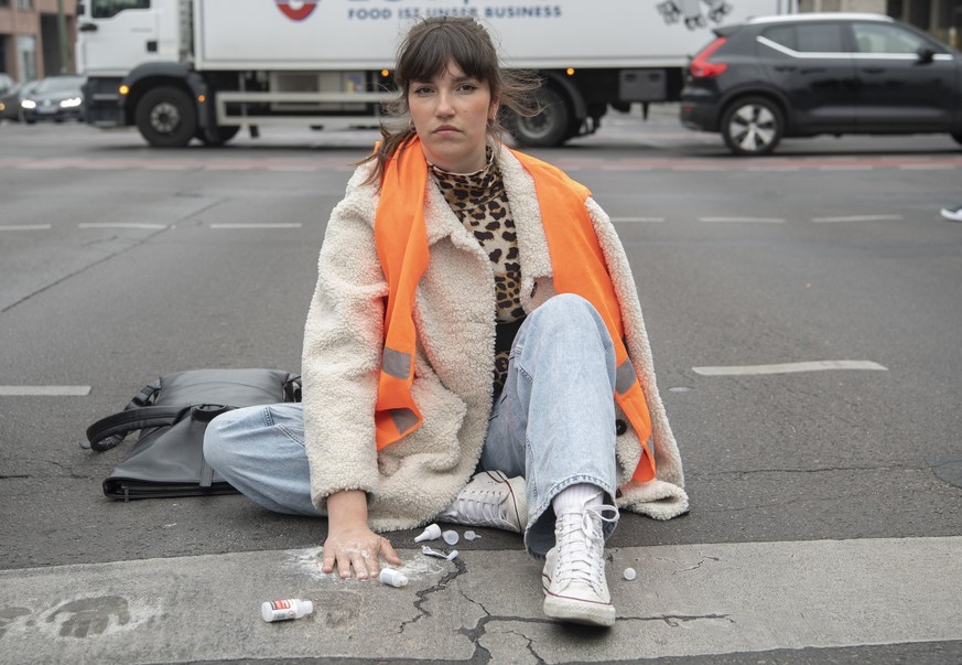 16.05.2023, Berlin: Carla Hinrichs, Sprecherin der Klimagruppe Letzte Generation, sitzt bei einer Straßenblockade der Letzten Generation mit einer auf den Asphalt festgeklebten Hand auf der Straße. Fo ...