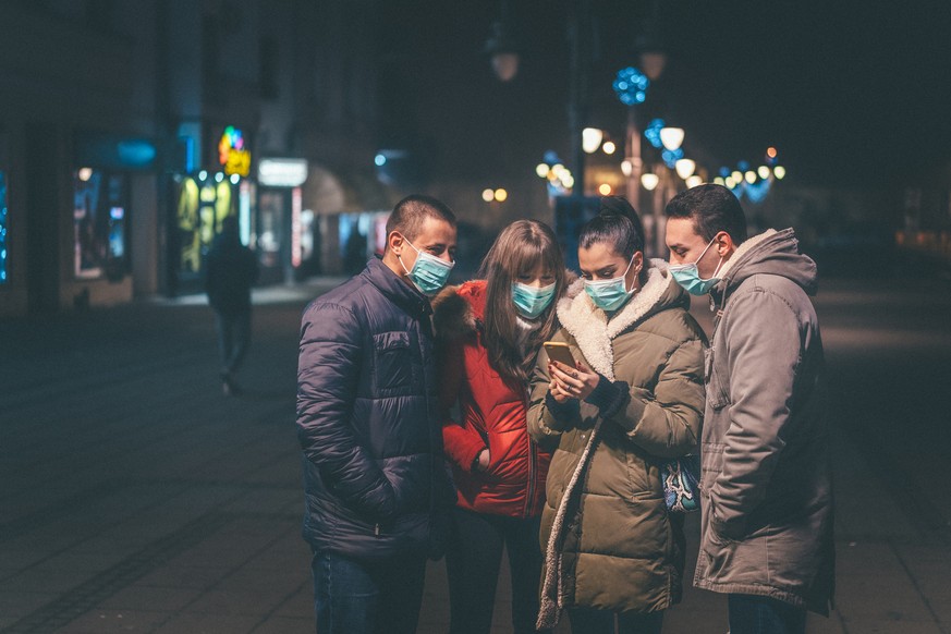 Group of young people with pollution masks on street using smartphone.