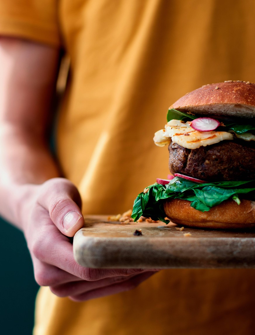 Cropped unrecognizable person holding delicious vegan lentils hamburgers placed on wooden board on dark background Copyright: xOlgaxVilax