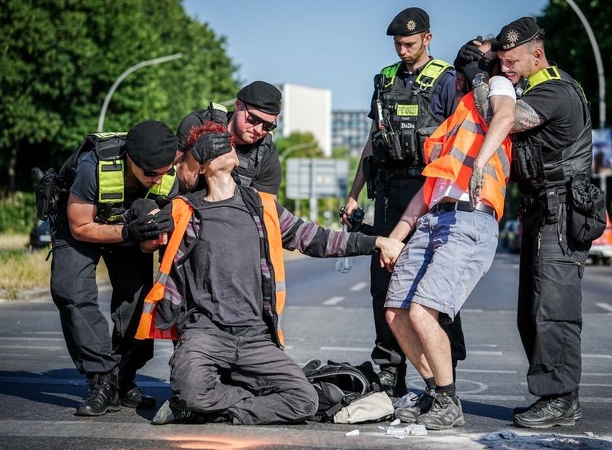 12.06.2023, Berlin: Aktivisten der Gruppe Letzte Generation werden bei einer Blockadeaktion am Großen Stern an der Siegessäule von der Polizei von der Straße entfernt. Sie klebten sich auf der Straße  ...