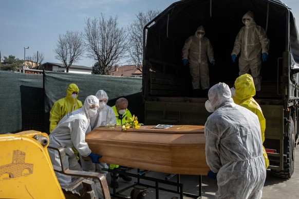 PONTE SAN PIETRO, ITALY - MARCH 28: Carabinieri officers, wearing protective suits, lift a coffin on March 28, 2020 in Ponte San Pietro, near Bergamo, Northern Italy. The Italian Army has been brought ...