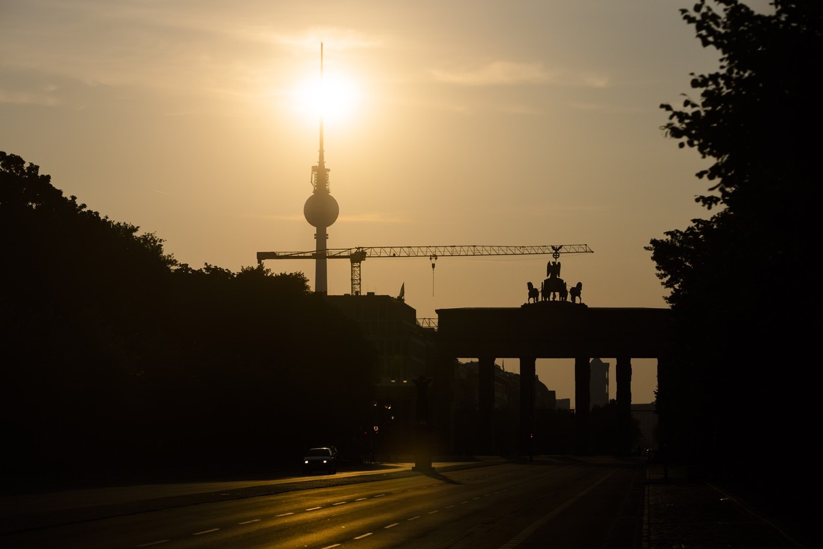 19.08.2023, Berlin: Das Brandenburger Tor und der Fernsehturm sind im Gegenlicht der aufgehenden Sonne zu sehen. Die Menschen in Berlin und Brandenburg müssen sich am Samstag auf starke bis extreme Wä ...