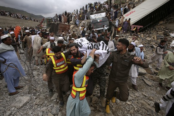 18.04.2023, Pakistan, Torkham: Rettungskräfte und Freiwillige tragen einen Leichnam, nachdem dieser aus den Trümmern des Erdrutsches geborgen wurde. Bei einem schweren Verkehrsunfall, verursacht durch ...