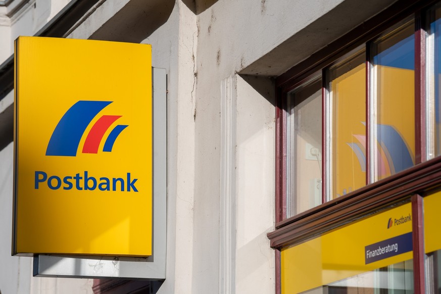 ARCHIV - 25.03.2019, Brandenburg an der Havel: Ein Schild mit dem Logo der Postbank ist an der Fassade einer Bankfiliale angebracht. Die Deutsche Bank verspricht Postbank-Kunden bei der anstehenden dr ...