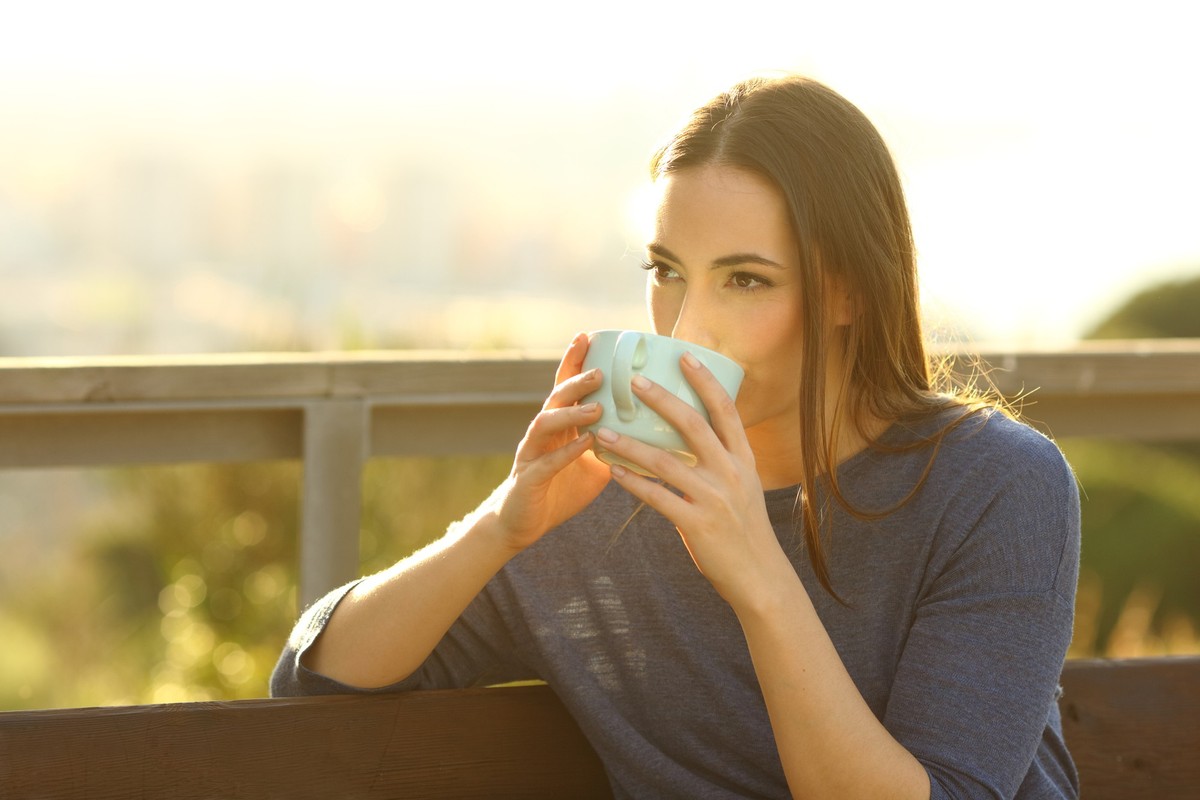 Woman drinking coffee in a park at sunset