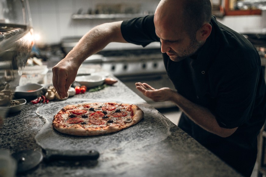 The main chef putting final ingredients on italian pizza in the restaurant
