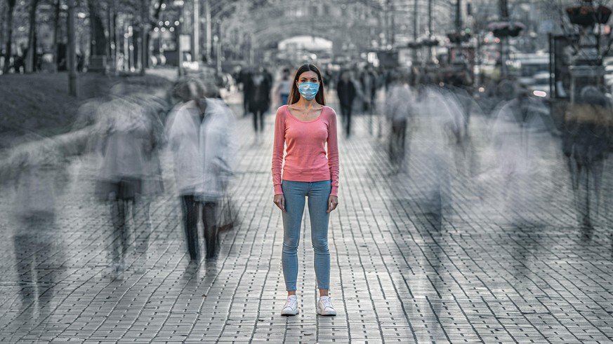 The young woman with medical mask on her face stands on the crowded street