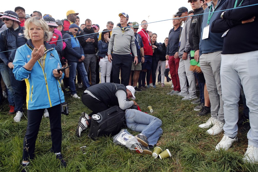A man tends an unidentified injured woman after she was hit by US player Brooks Koepka's ball on the 6th hole during a fourball match on the opening day of the 42nd Ryder Cup at Le Golf National in Sa ...