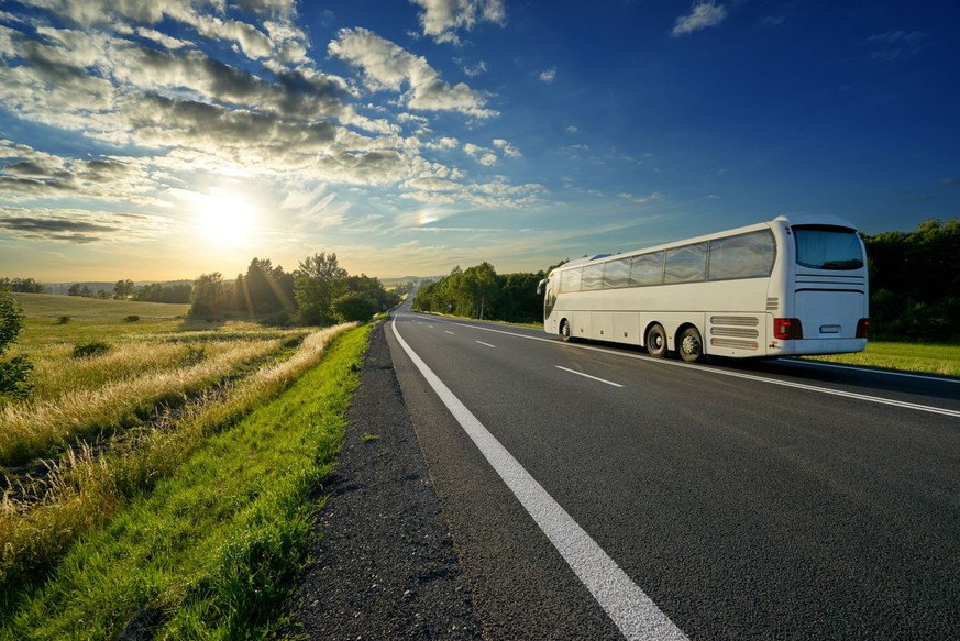 Weißer Bus Reisen auf der asphaltierten Straße in einer ländlichen Landschaft bei Sonnenuntergang