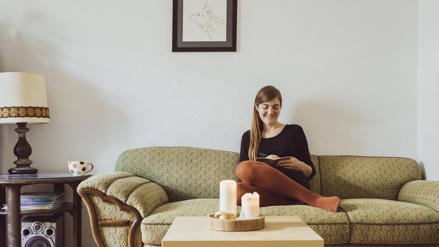 Woman sitting on couch in the living room writing in notebook model released Symbolfoto property released PUBLICATIONxINxGERxSUIxAUTxHUNxONLY JSCF00019