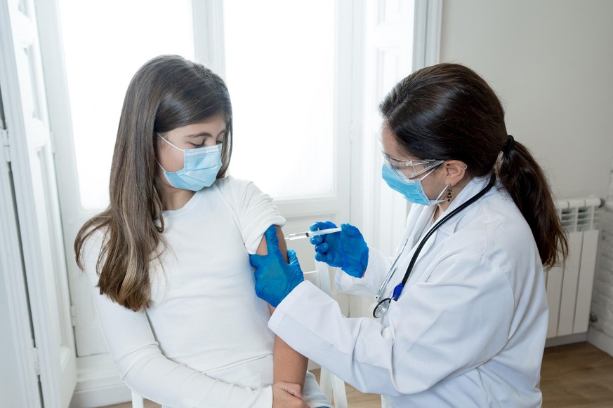 Nurse administering the coronavirus vaccine to a a young girl patient with face mask in Doctors clinic. Immunization, medical treatment and Covid-19 vaccination program after clinical trial in humans.