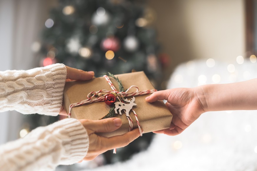 Female hands decorates Christmas gift box with dried orange and Christmas tree branch. Overhead view. Eco friendly Christmas package for holiday gifts.