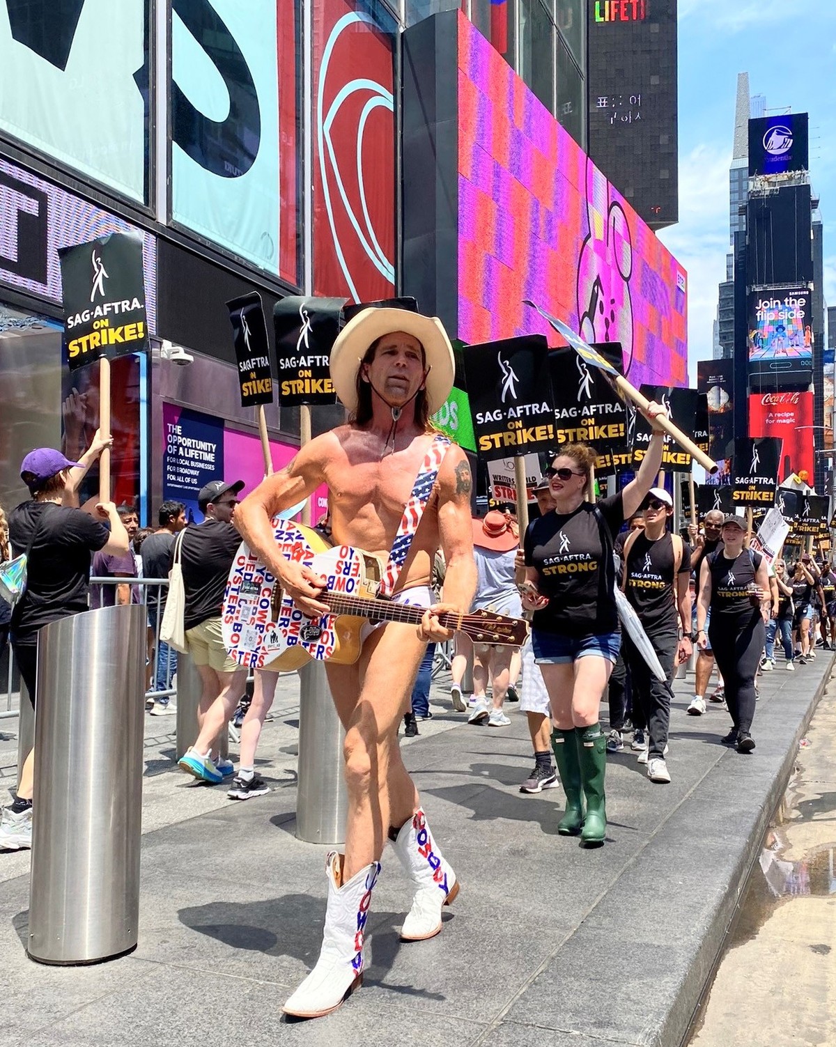 14.07.2023, USA, New York: Der Naked Cowboy protestiert mit Angehörigen der Gewerkschaft SAG-AFTRA am Times Square vor dem Rockefeller Center in New York für bessere Vergütung und Regelungen beim Eins ...