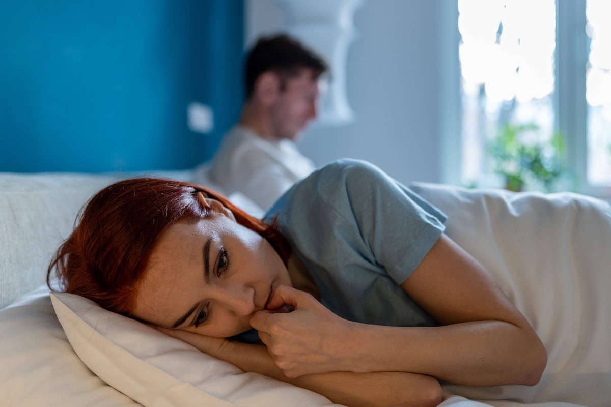 Upset wife lies with her back to husband. Man with disinterested look ignores sad depressed woman. Upset wife lies with her back to husband. Frustration, unhappiness, pain, resentment and thoughtfulne ...