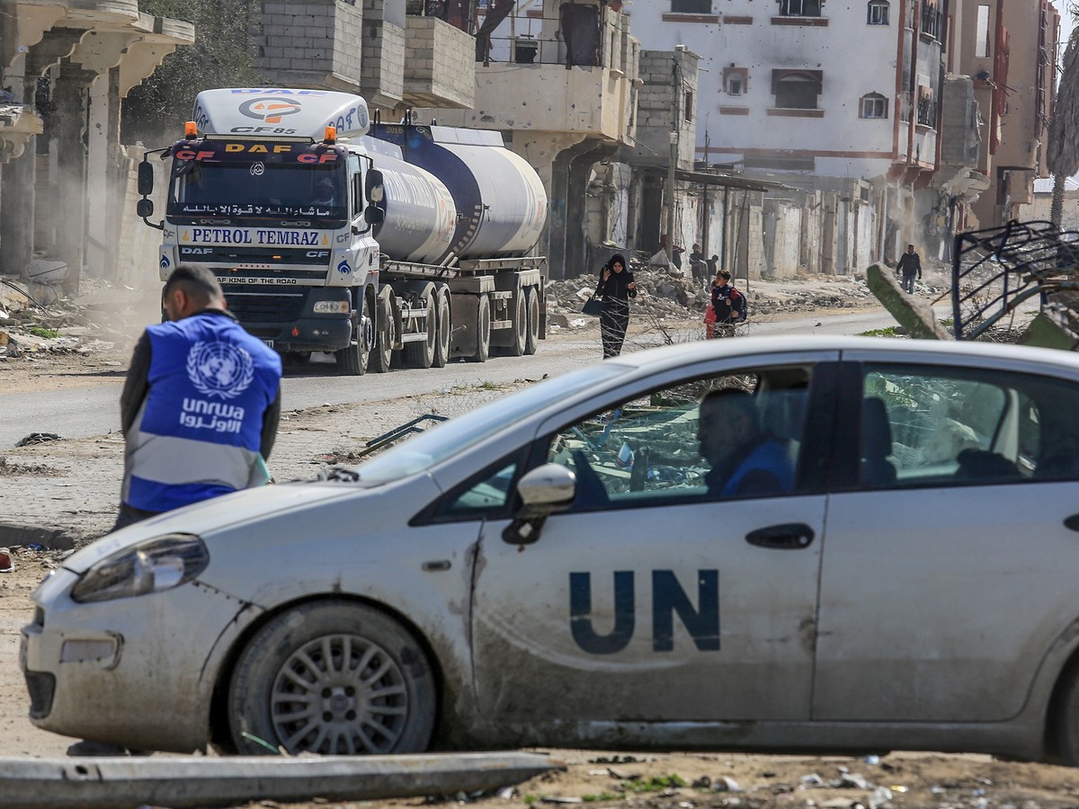 ARCHIV - 17.02.2025, Palästinensische Gebiete, Rafah: Ein UNRWA-Mitarbeiter lehnt an einem UN-Fahrzeug, während Lastwagen mit humanitärer Hilfe über den Grenzübergang Kerem Schalom in den Gazastreifen ...