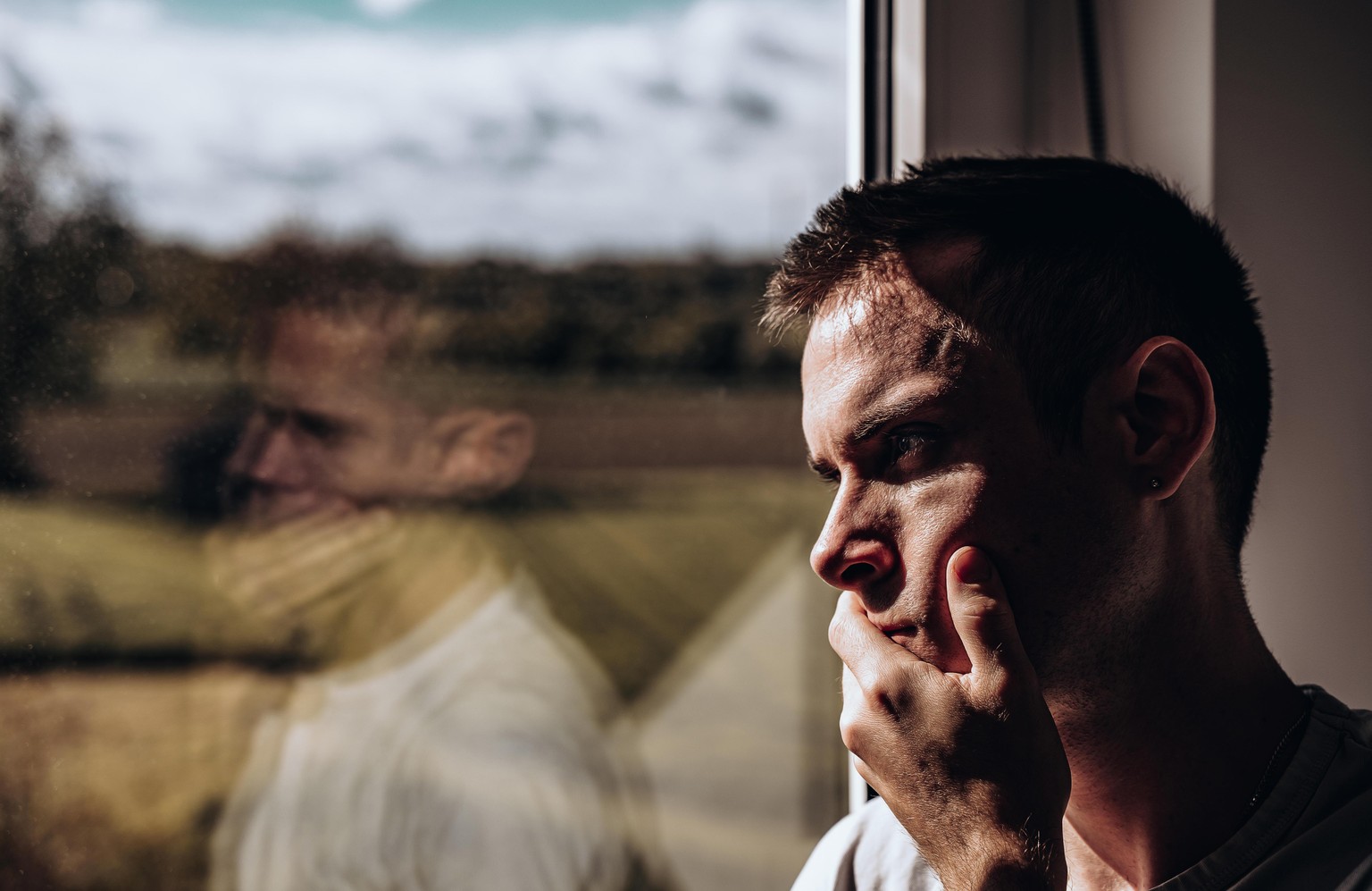 Nachdenklicher trauriger Mann schaut alleine durch das Fenster || Modellfreigabe vorhanden
