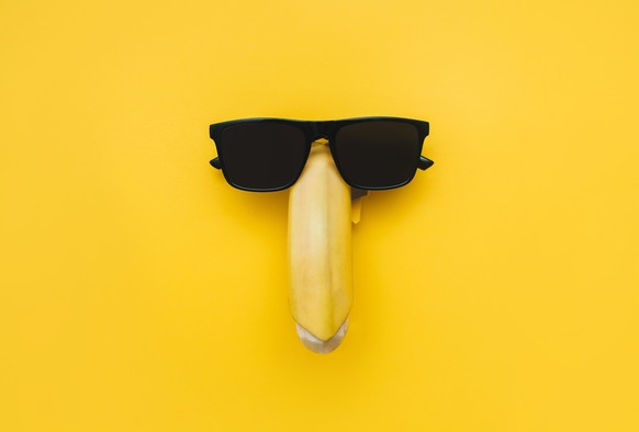 A fumnny banana with black sunglasses on a yellow paper background. Surveillance, detective, observer and spy concept. Copy space.