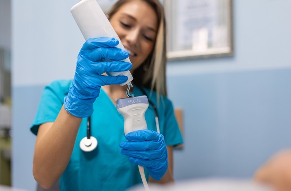 Smiling female doctor applying gel on ultrasound device before treatment. Hands in gloves apply a strip of transparent gel to the ultrasonic scanner sensor.
