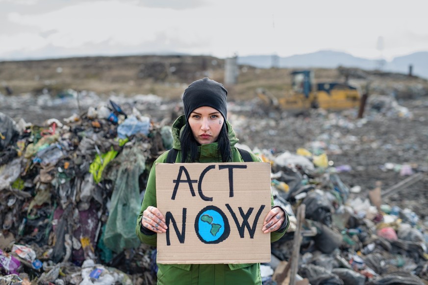 Woman activist holding placard poster on landfill, environmental pollution concept.