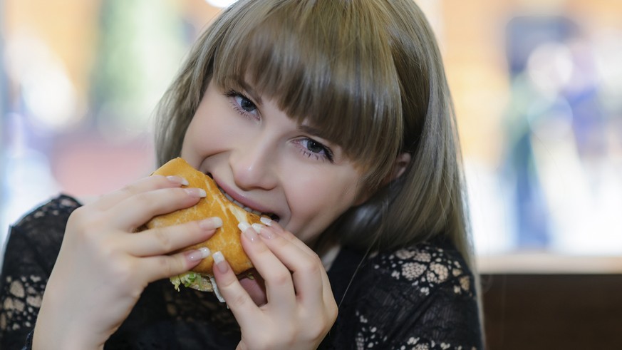 beautiful woman outdoors taking a bite from a burger.