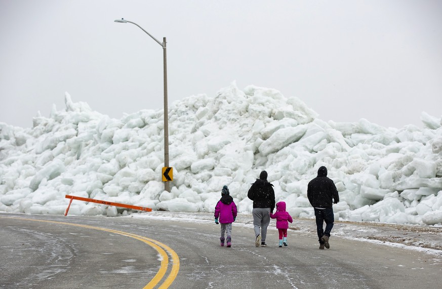 A family walks near a massive build up of ice that was pushed onto the shore of Mather Park in Fort Erie, Ont., Monday, February 25, 2019. A windstorm Sunday broke an ice boom in Lake Erie and allowed ...