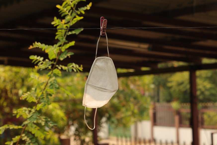 White mask hanging on the wire with plastic clip and sunlight, cleaning and reuse mask protection during CORONAVIRUS spread out and mask expensive