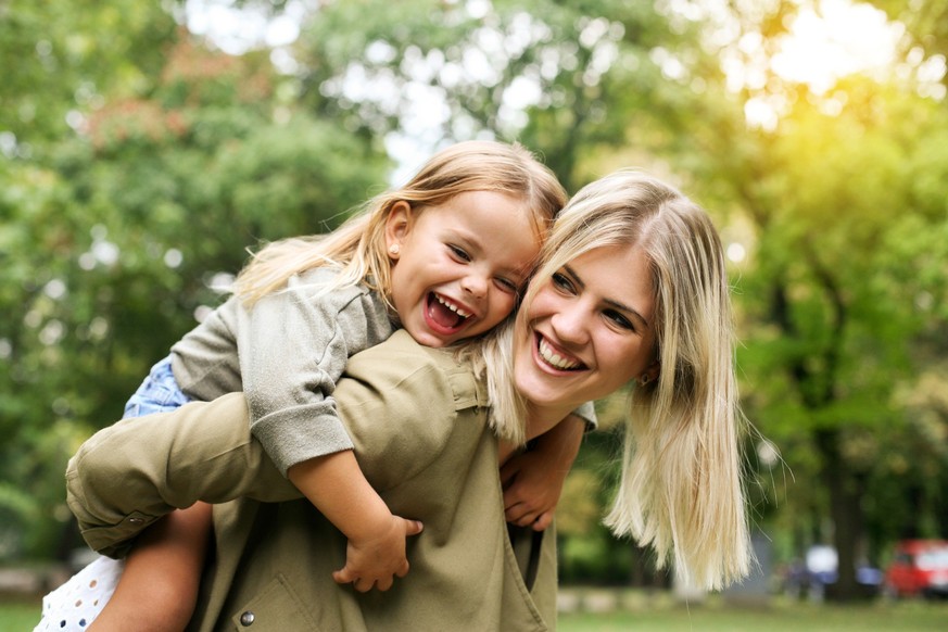 Cute young daughter on a piggy back ride with her mother.