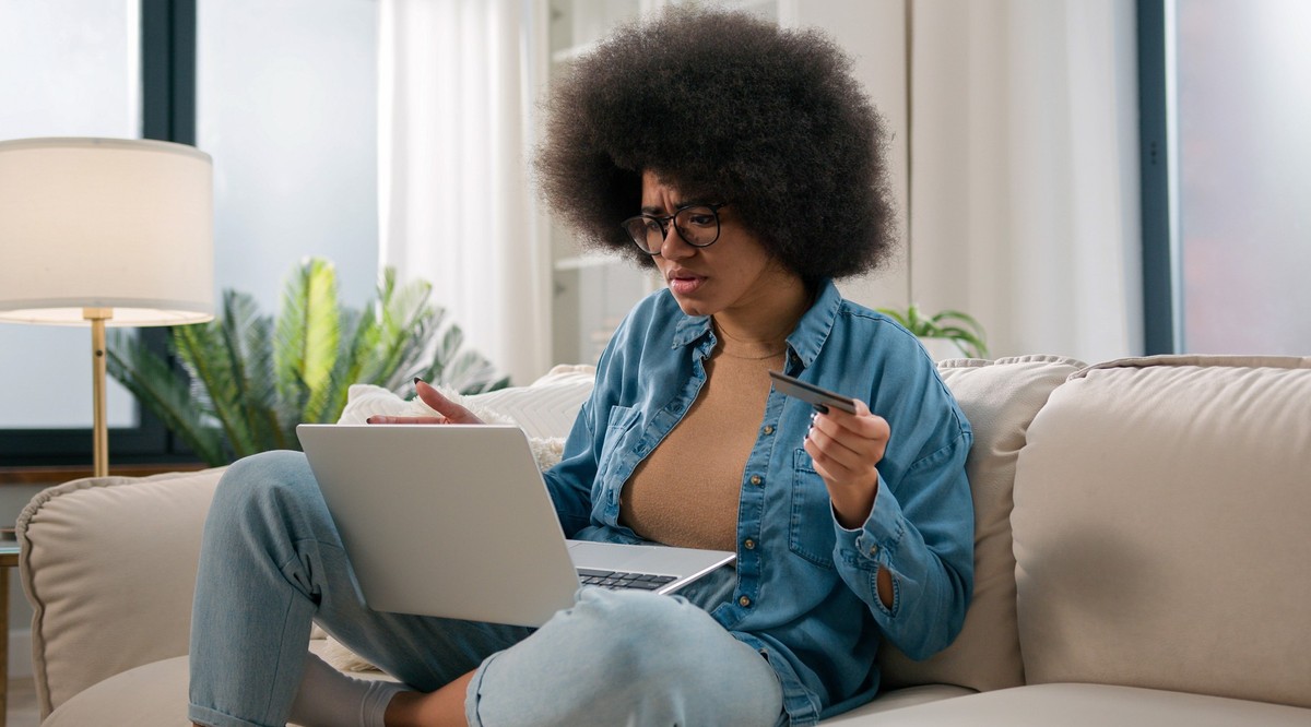 Confused puzzled irritated upset girl buyer African American woman try pay online with laptop credit card failure error mistake secure number shopping problem unsuccessful payment bank trouble at home ...