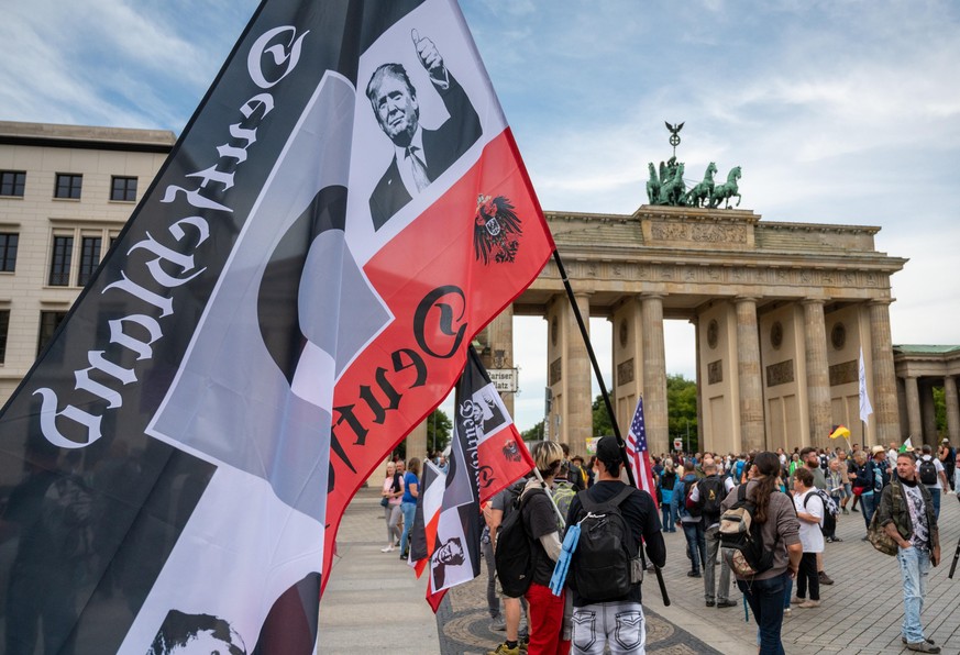 dpatopbilder - 29.08.2020, Berlin: Ein Demonstrant hält vor einer Demonstration gegen die Corona-Maßnahmen eine große Reichsflagge mit dem Konterfei von US-Präsident Donald Trump vor dem Brandenburger ...