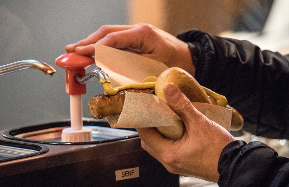 02.12.2022, Nordrhein-Westfalen, K�ln: Ein Besucher pumpt Senf auf eine Bratwurst im Br�tchen auf dem Weihnachtsmarkt am Dom in K�ln. Die Weihnachtsm�rkte sind vielerorts in Nordrhein-Westfalen �hnlic ...