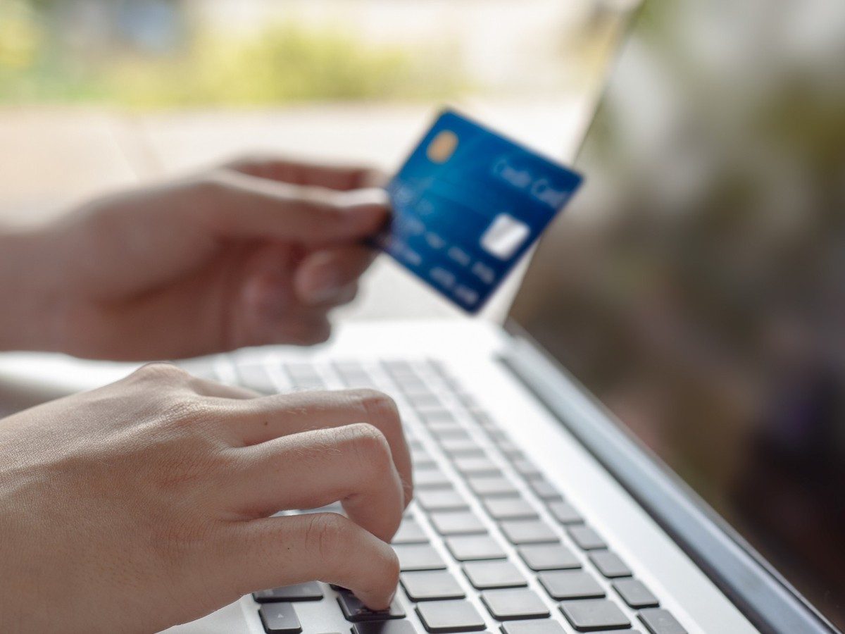 Woman hand holding blue credit card and using a modern laptop, typing and texting. against defocus green nature outdoor. mobile payment, online shopping concept