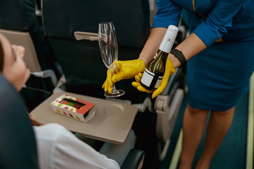 Close up of female flight attendant hands holding bottle of alcoholic drink and glass while woman sitting in passenger chair
