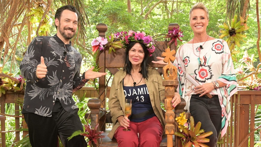 30.01.2023, Australien, Brisbane: Visagistin Djamila Rowe sitzt mit ihrer Krone nach dem Sieg beim RTL-Dschungelcamp 2023 auf ihrem Thron neben der Moderatorin Sonja Zietlow (r) und Moderator Jan Köpp ...