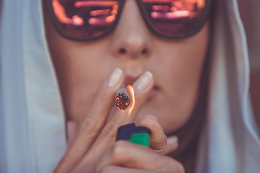 Young woman smoking marijuana joint - medical marijuana use and legalization of cannabis concepts - closeup-of lighting a weed cigarette in Amsterdam (Holland - Netherlands)